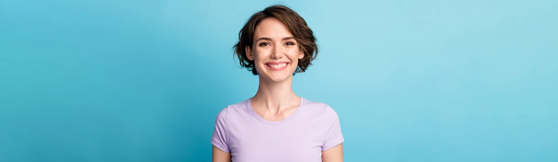 A woman with short hair, smiling in front of a teal wall.