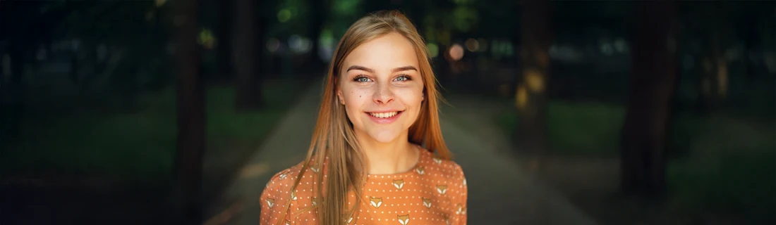 A woman smiling in a park with trees behind her.